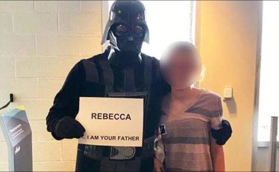 A father picks up his daughter while dressed as Darth Vader. 