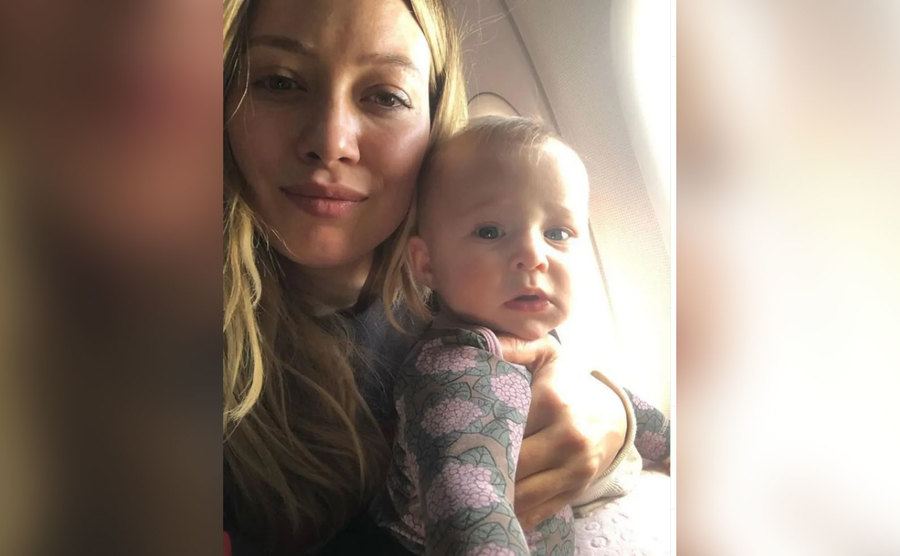 Hilary takes a selfie with her baby on an airplane. 