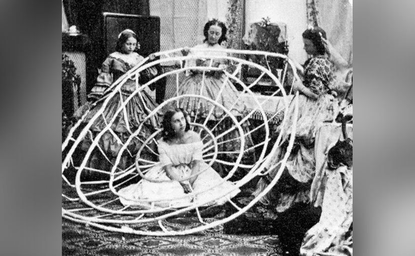A group of women helps another put on her dress hoops. 