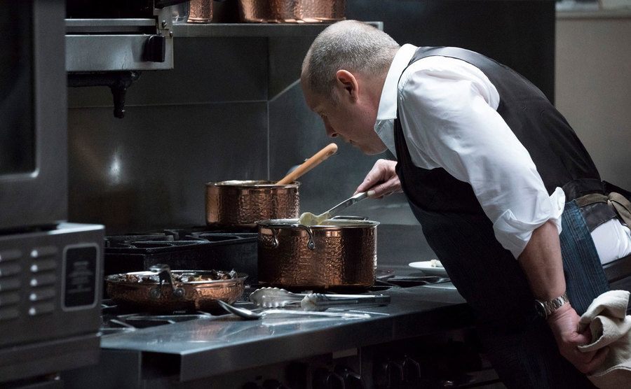 James Spader stands over a stove cooking in a still from The Blacklist. 